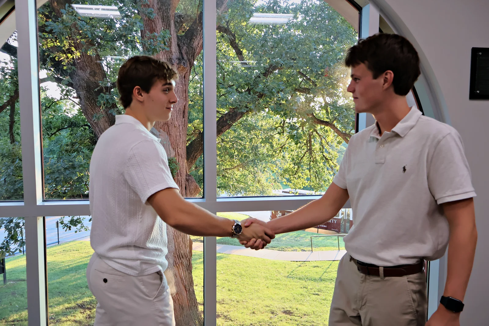 Jack Moutardier and Daxton Noe shaking hands by a window